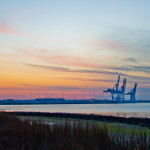 Pastel colored sunset over water with industrial shipping crane in background.