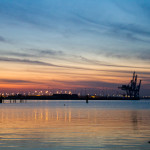 Sunset over water showing muted colors and an industrial crane.