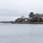 Monochromatic hues connect the winter sky to the frozen solid LaFayette River of the Larchmont neighborhood in Norfolk, Virginia. The trees, houses and dock stand out as a stark, dark contrast to the pale blue shades of the ice and foggy cloud cover.