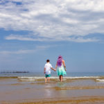 mother, son, holding hands, beach, ocean, clouds, purple hair, love, sunny, blue sky